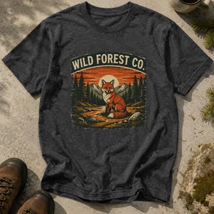 Könnte beinhalten: Ein anthrazitfarbenes Kurzarm-T-Shirt mit einem Grafikdruck eines Fuchses, der in einer Waldlandschaft mit Bergen und einer Sonne im Hintergrund sitzt. Der Text WILD FOREST CO. ist in einem Bogen über der Fuchsillustration gedruckt.