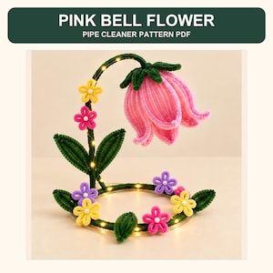 Peut inclure: Un projet artisanal intitulé PINK BELL FLOWER PIPE CLEANER PATTERN PDF représentant une fleur en cloche rose faite de cure-pipes sur une tige verte avec de petites fleurs colorées et des perles blanches, illuminée par des guirlandes lumineuses.