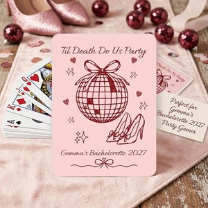 May include: A light pink rectangular card featuring dark red line art of a disco ball with a bow, a pair of high heels, hearts, and stars. The text reads Til Death Do Us Party and Gemma's Bachelorette 2027. The card is part of a deck of playing cards.