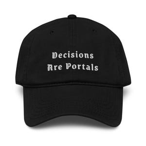 Könnte beinhalten: Eine schwarze Baseballkappe mit dem gestickten weißen Text "Decisions Are Portals" in einer gotischen Schriftart, die mittig auf der Vorderseite platziert ist. Die Kappe hat eine strukturierte Krone, einen gebogenen Schirm und einen Knopf oben.