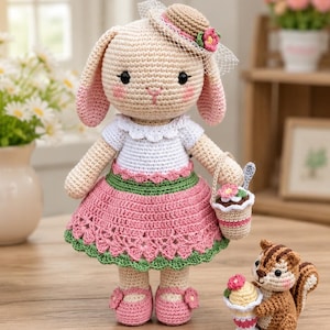 May include: A crochet rabbit doll with long ears, wearing a beige hat with a pink flower, a white top, and a pink and green skirt. The rabbit holds a small basket with a flower. Beside it stands a small brown squirrel holding a dessert cup.