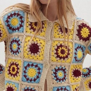 May include: A long-sleeve crochet cardigan featuring a granny square pattern in shades of yellow, light blue, and dark maroon, bordered by beige yarn. The garment includes a classic collar and a front button closure with matching beige buttons.