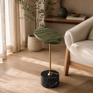 May include: A side table featuring an oval-shaped green marble top supported by a slender gold-toned metal stem and a cylindrical black marble base with white veining, standing as a singular piece of furniture with a polished stone finish.