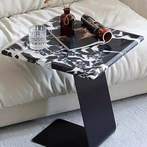 Side angle view of modern marble side table featuring natural black and white marble slab with sturdy black steel base, luxury living room accent table, handmade marble end table, minimalist furniture for modern interiors.