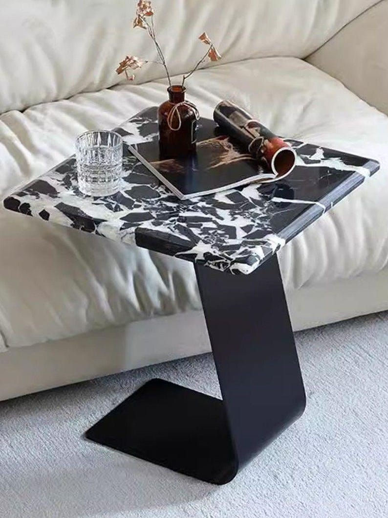 Side angle view of modern marble side table featuring natural black and white marble slab with sturdy black steel base, luxury living room accent table, handmade marble end table, minimalist furniture for modern interiors.
