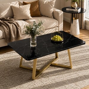 May include: A rectangular coffee table with a black faux marble top featuring white veining and a gold-toned metal frame. A clear glass vase with green foliage and a gold wire basket containing green grapes sit on the table surface.