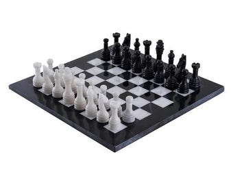 Puede incluir: Un tablero de ajedrez cuadrado con un patrón de cuadros alternos en piedra blanca y negra. El tablero está dispuesto con un conjunto completo de piezas de ajedrez talladas, con un lado en color blanco sólido y el lado opuesto en color negro sólido.