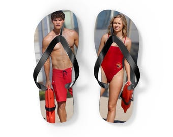 May include: A pair of flip-flops featuring a photographic print of a lifeguard in red swim trunks on the left sandal and a lifeguard in a red one-piece swimsuit on the right sandal. Both sandals have black straps and show red rescue buoys.