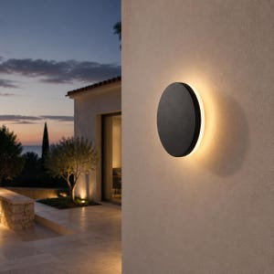 Peut inclure: Une applique murale circulaire au fini noir mat, émettant une lumière chaude et rayonnante depuis l'arrière du disque, créant un effet de halo doux sur le mur extérieur beige texturé d'un bâtiment à la tombée de la nuit.