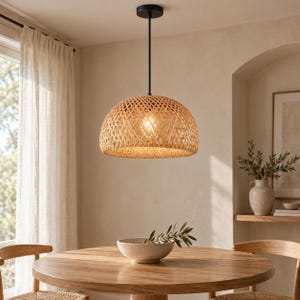 Pode incluir: Uma luminária pendente em forma de cúpula com uma cúpula de bambu ou vime trançado em tom castanho claro. A luminária está suspensa no teto por uma haste preta fina e uma canopla circular preta, emitindo um brilho quente da lâmpada.