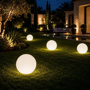 Peut inclure: Quatre lampes d'extérieur sphériques diffusant une lumière blanche et chaude sont disposées sur une pelouse verte. Chaque lampe ronde et lisse émet une lueur douce, créant un cercle lumineux sur l'herbe dans un jardin en soirée.