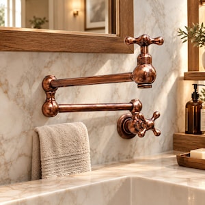 May include: A wall-mounted pot filler faucet with a metallic copper finish, featuring a double-jointed articulating arm and a cross-handle design. The fixture is installed on a white marble wall above a sink, with a beige towel hanging nearby.