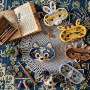 Peut inclure: Une collection de six porte-lunettes en crochet en forme d'animaux, comprenant un lapin blanc, une girafe jaune, un chien bleu, un cerf marron, un chien multicolore et un raton laveur gris, conçus pour maintenir des lunettes sur le visage.