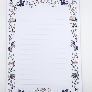 Könnte beinhalten: Ein weißes Blatt liniertes Briefpapier mit einem dekorativen Rand aus dunkelgrünen Ranken, violetten Drachen, Einhörnern, offenen Büchern, Regenbögen, gelben Mondsicheln, rosa Herzen und kleinen Sternen, die symmetrisch um die Seitenränder angeordnet sind.