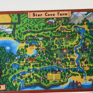 Puede incluir: Una alfombrilla de escritorio rectangular con un mapa en pixel art de Star Cove Farm que muestra paisajes verdes, ríos y edificios. Un personaje llamado Crystal con un lazo rojo aparece en la esquina. Un ratón rosa claro está a la izquierda.
