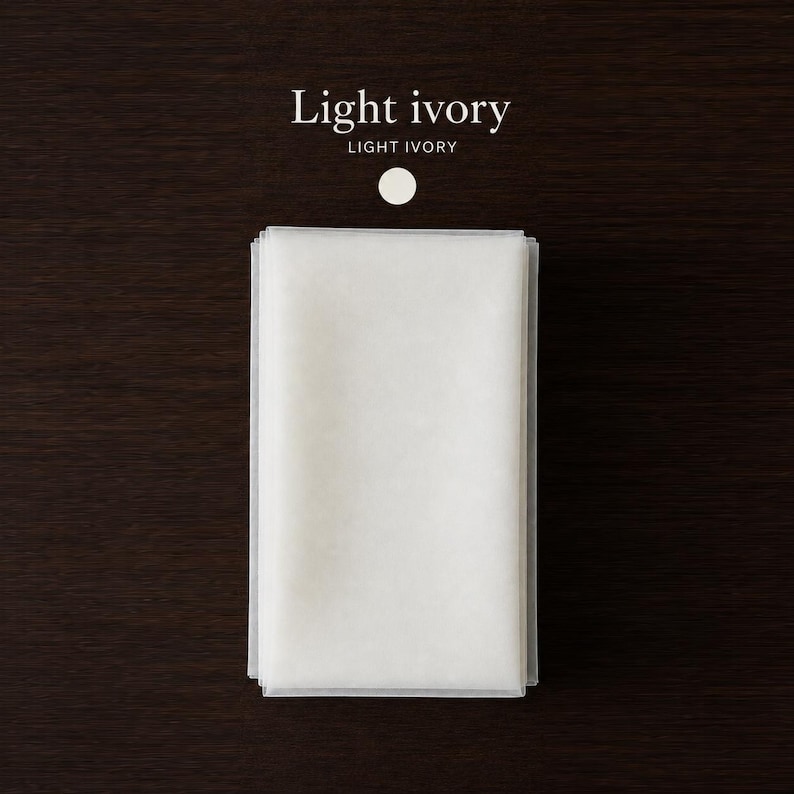 May include: A rectangular piece of light ivory fabric folded into a neat stack. Above the fabric, the text reads Light ivory in a serif font, followed by the text LIGHT IVORY in a sans-serif font and a small light ivory circular icon.