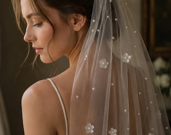May include: A sheer white bridal veil crafted from fine tulle, embellished with scattered small white pearls and delicate, translucent five-petaled floral appliqués. The lightweight fabric drapes gracefully, featuring a soft texture and a clean, minimalist aesthetic.