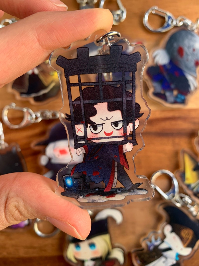 K&ouml;nnte beinhalten: Ein durchsichtiger Acryl-Schl&uuml;sselanh&auml;nger mit einer Comicfigur mit schwarzen Haaren, einem rot-schwarzen Outfit und einem K&auml;fig &uuml;ber dem Kopf. Die Figur h&auml;lt den K&auml;fig mit beiden H&auml;nden und hat einen schelmischen Gesichtsausdruck. Der Schl&uuml;sselanh&auml;nger ist von anderen Schl&uuml;sselanh&auml;ngern mit verschiedenen Comicfiguren umgeben.