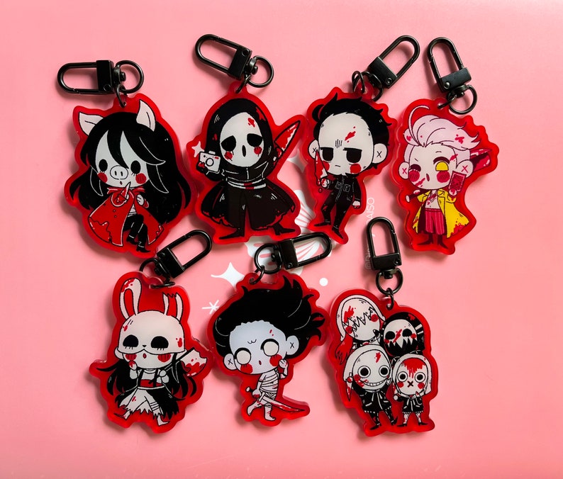 May include: Set of 8 colorful cartoon character keychains with black metal rings. The characters are drawn in a cute, stylized, and slightly creepy style. The characters are all wearing red, white, and black clothing.