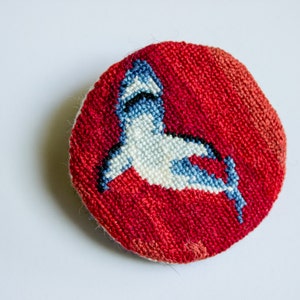 May include: A round, red needlepoint cushion with a white and blue embroidered shark design.