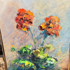 May include: An oil painting in a thin gold frame depicting two vibrant orange and red geranium flowers with thick, textured brushstrokes. The stems and leaves are rendered in shades of green, set against a light, neutral, and abstract background.