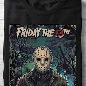 Może przedstawiać: Czarny t-shirt z grafiką przedstawiającą postać w masce hokejowej w ciemnym, zalesionym otoczeniu. Napis "FRIDAY THE 13TH" jest nadrukowany u góry przetartą czcionką, a liczba 13 jest wyróżniona kolorem czerwonym.