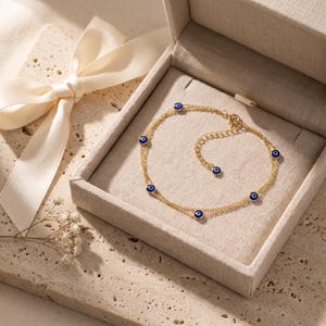 Pode incluir: Uma delicada pulseira de corrente em tom dourado com vários pequenos berloques circulares de olho grego com centros azuis, brancos e pretos. A pulseira inclui uma fina corrente extensora com um berloque de olho grego a condizer na ponta.