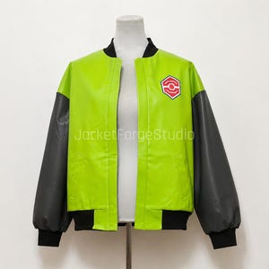 Könnte beinhalten: Eine lindgrüne und dunkelgraue Bomberjacke mit schwarzem Rippstrickkragen und Bündchen. Die Jacke hat eine glatte Oberfläche und zeigt ein rotes und weißes sechseckiges Emblem auf der linken Brust. Der Text JacketForgeStudio ist sichtbar.