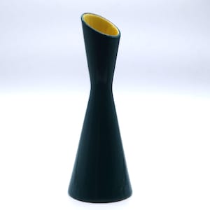 May include: A tall, slender ceramic vase with a dark forest green exterior and a contrasting bright yellow interior. The vase features a wide, conical base that tapers inward towards the middle before flaring slightly at the angled top opening.