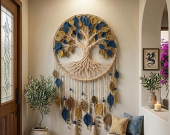 May include: A circular macrame wall hanging featuring a tree of life design with cream-colored cord, accented by numerous blue and gold crocheted leaves. The piece includes hanging strands with additional leaves, tassels, and blue beads.