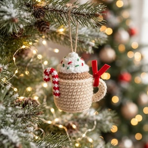 May include: A crocheted Christmas ornament shaped like a beige mug filled with white whipped cream and colorful sprinkles. A red and white striped candy cane is attached to the side, and a small red velvet ribbon is tied to the mug handle.