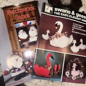 May include: Two craft pattern booklets. The left booklet is titled Patchwork Santa by LuAnn Stout, featuring images of fabric Santa dolls. The right booklet is titled swans & geese THE EASY, ELEGANT ONES by Lynn Paulin and Elizabeth Capstick.