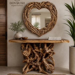 May include: A heart-shaped mirror framed with natural driftwood pieces mounted above a console table. The table features a smooth, flat wooden top supported by a base constructed from a large, intricate, gnarled tree root system.