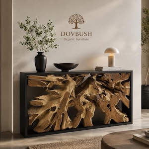 May include: A rectangular console table featuring a black frame and a natural, raw teak root wood centerpiece. The top surface holds a black vase with green branches, a black bowl, a white table lamp, and a book. The wall displays the DOVBUSH logo.