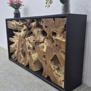 May include: A rectangular console table featuring a matte black frame enclosing a natural, light brown teak root wood sculpture. The top surface holds a small black vase with pink tulips and a clear glass vase containing white and purple orchids.