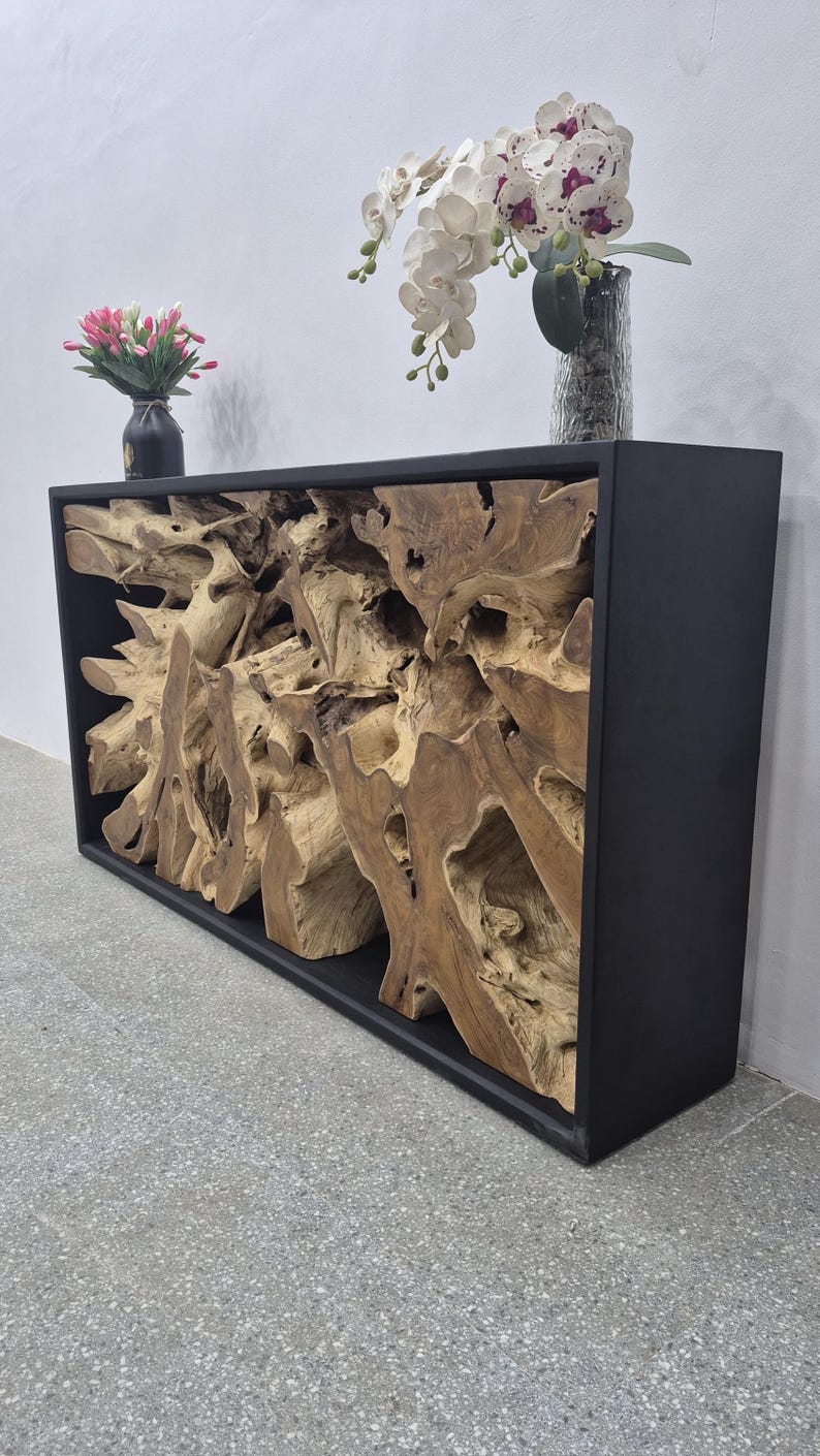 May include: A rectangular console table featuring a matte black frame enclosing a natural, light brown teak root wood sculpture. The top surface holds a small black vase with pink tulips and a clear glass vase containing white and purple orchids.