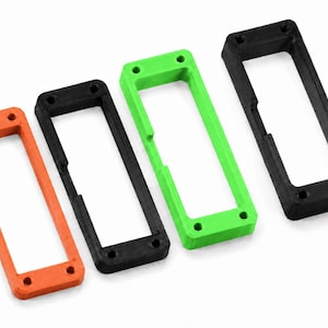 May include: Four rectangular frames arranged in a row, featuring one orange, two black, and one bright green unit. Each frame has a hollow center and four small circular mounting holes, one located at each corner of the rectangular structure.