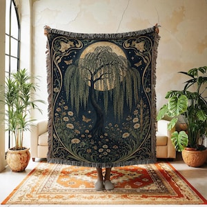 May include: A woven throw blanket featuring a dark blue background with a central weeping willow tree under a large full moon. The design includes surrounding floral patterns, butterflies, and stars with a fringed edge on the top and bottom.