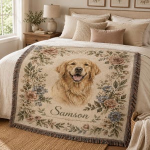 Custom pet portrait throw blanket laid across bed with woven floral details, fringe edge, and personalized dog name.