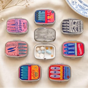 Puede incluir: Una colección de ocho pastilleros rectangulares de metal con esquinas redondeadas, con coloridos diseños gráficos de sardinas. Un pastillero abierto en el centro muestra el texto AMANDA'S PILL BOX y contiene varias pastillas pequeñas blancas y azules.