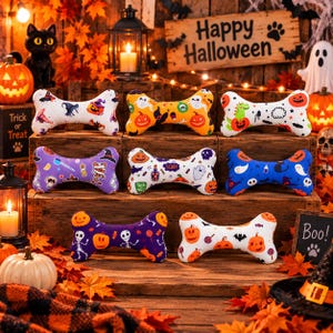 Könnte beinhalten: Acht Plüsch-Hundespielzeuge in Knochenform mit verschiedenen Halloween-Motiven wie Kürbissen, Geistern, Skeletten und Fledermäusen. Die Spielzeuge sind auf Holzkisten angeordnet und zeigen farbenfrohe Drucke in Weiß, Orange, Lila und Blau.