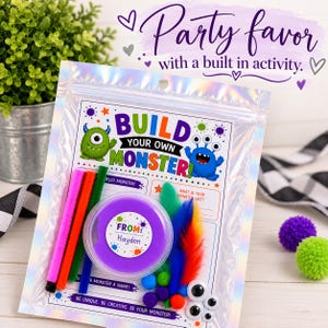 May include: A Build Your Own Monster craft kit in a holographic pouch. The kit includes a container of purple putty labeled From Hayden, colorful pipe cleaners, feathers, and googly eyes. The card features monster graphics and text prompts.