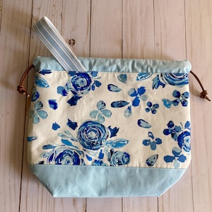 May include: A blue and white drawstring bag with a floral pattern. The bag has a light blue lining and a brown leather drawstring.