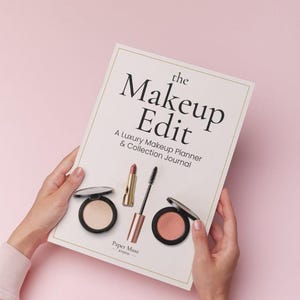 Op de afbeelding: Een witte rechthoekige planner met de titel The Makeup Edit: A Luxury Makeup Planner & Collection Journal. De kaft bevat illustraties van een poedercompact, een lippenstift, een mascara en een blushcompact. Paper Muse Studio staat onderaan.