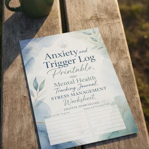 May include: A printed Anxiety and Trigger Log Mental Health Tracking Journal Stress Management Worksheet with blue and green watercolour leaf illustrations, featuring lines for date, time, triggers, and a checklist for emotional strategies used.