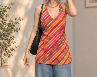 Könnte beinhalten: Ein ärmelloses Neckholder-Top mit einem lebendigen diagonalen Streifenmuster in Pink, Orange und Olivgrün, kombiniert mit einer weiten blauen Jeans und einer schwarzen Umhängetasche. Das Top hat einen tiefen V-Ausschnitt und eine körpernahe Passform.