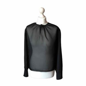 Op de afbeelding: Zwarte doorschijnende blouse met lange mouwen, een ronde hals en een klein decoratief detail bij de kraag. De blouse wordt getoond op een witte mannequin, die de vloeiende stof en het ontwerp laat zien. De mouwen hebben een manchet.