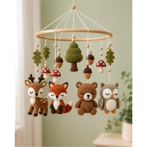 May include: A hanging mobile featuring crocheted woodland animals including a deer, fox, bear, and owl, interspersed with crocheted trees, acorns, and mushrooms suspended from a circular wooden frame by white strings and wooden beads.
