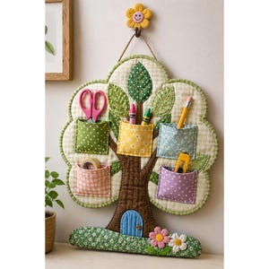 May include: A quilted wall organizer shaped like a tree with a brown trunk and a light green gingham canopy. It features five fabric pockets in green, yellow, blue, pink, and purple, holding scissors, crayons, a pencil, tape, and a utility knife.