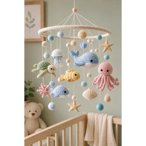 May include: A hanging mobile featuring crocheted sea creatures including a blue whale, pink octopus, green turtle, yellow fish, and jellyfish. The mobile includes small beige and blue felted balls and two beige starfish suspended from a circular frame.
